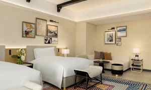 Hotellihuone, jossa on kaksi sänkyä, sohva ja koristeellisia maalauksia seinällä. (Tekoälyn luoma teksti)