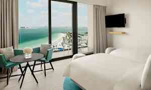 Hotellihuone, jossa kaksi sänkyä, pöytä ja tuolit sekä näkymä rannalle ja merelle. (Tekoälyn luoma teksti)