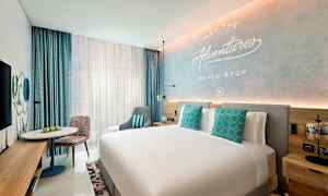 Moderni hotellihuone, jossa on suuri sänky, koristeelliset tyynyt, oleskelutila ja kirjoituspöytä. (Tekoälyn luoma teksti)