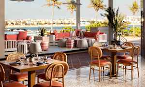 Ulkoterassi, jossa pöytiä ja tuoleja, sohvat ja näkymä vedelle ja taloille. (Tekoälyn luoma teksti)