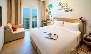 Hotellihuone, jossa on iso sänky, istumapaikka ja avoin ikkuna merinäköalalla. (Tekoälyn luoma teksti)