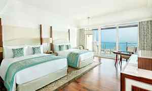 Hotellihuone, jossa on kaksi suurta sänkyä, vaalea sisustus ja merinäköala parvekkeelta. (Tekoälyn luoma teksti)