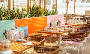 Ulkoterassi, jossa katettuja pöytiä, värikkäitä tyynyjä ja vehreyttä. (Tekoälyn luoma teksti)