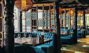 Ravintolan sisustus, jossa on turkooseja sohvia, koristeellisia pilareita ja puupaneeleja. (Tekoälyn luoma teksti)