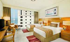 Hotellihuone, jossa kaksi yhden hengen vuodetta, kirjoituspöytä ja suuret ikkunat. (Tekoälyn luoma teksti)