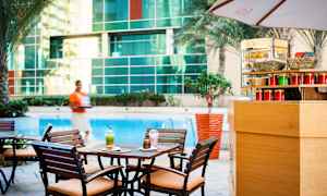 Kahvilapöytä, jossa on kaksi juomaa ja leivonnainen uima-altaan äärellä, ympärillä puita ja lasiseinä. (Tekoälyn luoma teksti)