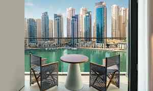 Näkymä parvekkeelta turkoosin veden äärelle, jota ympäröivät modernit korkeakerrostalot. Parvekkeella on pöytä ja kaksi tuolia. (Tekoälyn luoma teksti)