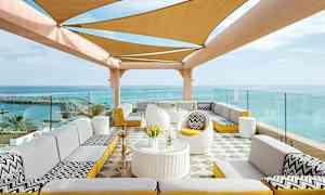 Ulkoterassi, jossa on istuma-alueita ja kangasvarjostin merenäkymän edessä. (Tekoälyn luoma teksti)