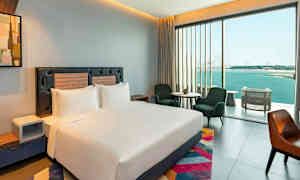 Moderni hotellihuone, jossa on suuri sänky, istumapaikkoja ja iso ikkuna merinäköalalla. (Tekoälyn luoma teksti)