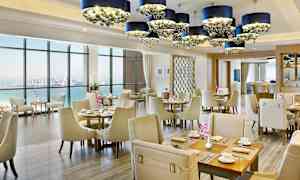 Tyylikkään ravintolan sisustus merinäköalalla, vaaleat huonekalut ja koristeelliset kattokruunut. (Tekoälyn luoma teksti)