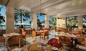 Ravintola, jossa puisia kalusteita ja näkymä rannalle suurten aukkojen kautta. (Tekoälyn luoma teksti)