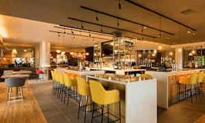 Baari, jossa on moderneja huonekaluja ja hyvin täytetty hylly pulloja. (Tekoälyn luoma teksti)