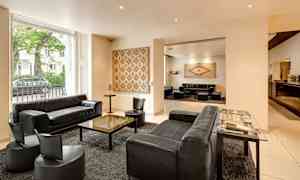 Tyylikäs hotellihuone mustilla sohvilla ja nojatuoleilla, keskellä pöytä ja seinillä taideteoksia. (Tekoälyn luoma teksti)