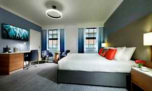 Hotellihuone, jossa on suuri sänky, kirjoituspöytä ja istuimet. (Tekoälyn luoma teksti)