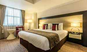 Hotellihuone, jossa on suuri sänky, koristeelliset tyynyt, lamput ja huonekaluja. (Tekoälyn luoma teksti)