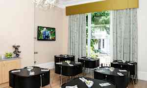 Vaalea huone, jossa on useita tummia pöytiä ja tuoleja sekä suuri ikkuna viheralueelle. (Tekoälyn luoma teksti)