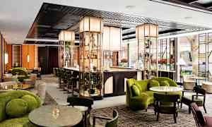 Kuva modernista hotellibaarista, jossa on tyylikkäät huonekalut ja vihreitä koristeita. (Tekoälyn luoma teksti)