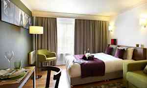 Hotellihuone, jossa on parivuode violeteilla ja valkoisilla vuodevaatteilla, vihreä tuoli ja ruokapöytä astioineen. (Tekoälyn luoma teksti)