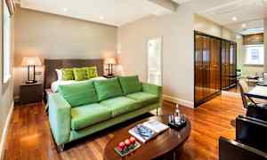 Hotellihuone vihreillä huonekaluilla, suuri sänky, puupöytä ja peilejä. (Tekoälyn luoma teksti)