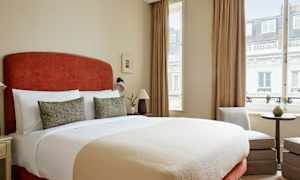 Makuuhuone, jossa suuri sänky, kaksi koristeellista tyynyä, lamput sivuilla ja ikkunat verhoilla. (Tekoälyn luoma teksti)