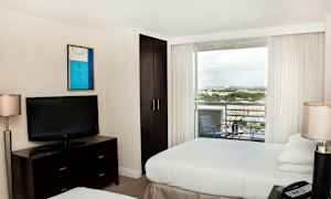 Hotellihuone, jossa kaksi sänkyä, televisio lipaston päällä, vaatekaappi ja parveke näkymällä. (Tekoälyn luoma teksti)