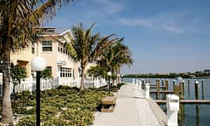 Kävelytie, johon kuuluu penkkejä ja lamppuja, on palmujen ympäröimä ja kulkee rakennuksen ohi pieneen venesatamaan. (Tekoälyn luoma teksti)