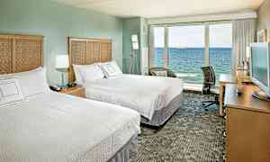 Hotellihuone, jossa on kaksi parivuodetta, televisio kirjoituspöydällä ja suuri lasiseinä, josta on näkymä merelle. (Tekoälyn luoma teksti)