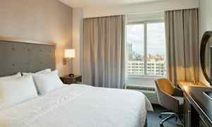 Hotellihuone, jossa on suuri sänky, työpöytä tuoleineen ja näkymä ikkunasta ulos. (Tekoälyn luoma teksti)