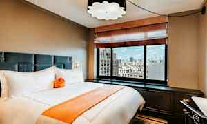 Tyylikäs hotellihuone, jossa on sänky, suuret ikkunat ja kaupungin näkymä. (Tekoälyn luoma teksti)