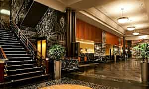 Kuva hotellin aulasta, jossa on marmodilattia, portaat, sohvia ja kasveja. (Tekoälyn luoma teksti)