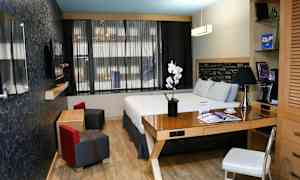 Moderni hotellihuone, jossa on parivuode, työpöytä ja oleskelualue. (Tekoälyn luoma teksti)