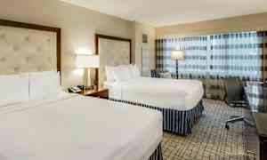 Hotellihuone, jossa on kaksi parivuodetta, lamppu ja työpöytä tuolin vieressä. (Tekoälyn luoma teksti)