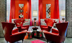 Tyylikkäästi sisustettu huone, jossa on punaisia nojatuoleja, metallisia pöytiä ja lamppuja sekä punaiset verhot ja nykyaikaisia peilejä seinillä. (Tekoälyn luoma teksti)