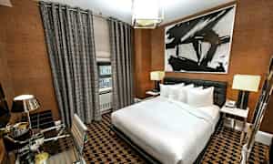 Hotellihuone, jossa moderni sisustus, suuri sänky, kirjoituspöytä ja abstraktia taidetta seinällä. (Tekoälyn luoma teksti)