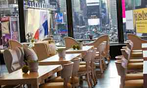 Ravintola, jossa on puiset pöydät ja tuolit sekä näkymä kaupungin neonvaloisiin näyttöihin. (Tekoälyn luoma teksti)