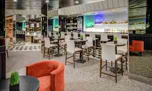 Modernin baarin sisustus, jossa on korkeita tuoleja pyöreiden pöytien ääressä ja taustalla baaritiski. (Tekoälyn luoma teksti)