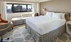 Hotellihuone, jossa suuri sänky ja ikkuna kaupunkinäkymällä. (Tekoälyn luoma teksti)