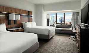 Hotellihuone, jossa on kaksi parivuodetta, istuinryhmä, kirjoituspöytä ja televisio, näkymä kaupunkiin ikkunan kautta. (Tekoälyn luoma teksti)