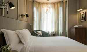 Tyylikäs makuuhuone, jossa suuri sänky valkoisilla lakanoilla, vihreä nojatuoli ja pehmeät verhot, jotka päästävät valoa. (Tekoälyn luoma teksti)