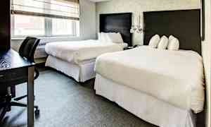 Hotellihuone, jossa on kaksi suurta sänkyä, kirjoituspöytä ja luonnonvaloa ikkunasta. (Tekoälyn luoma teksti)