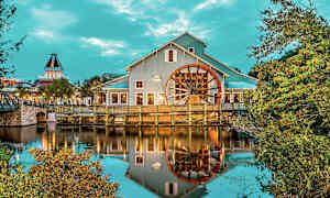 Rakennus, jossa on suuri pyörä veden äärellä, ympärillä puita ja kasveja. (Tekoälyn luoma teksti)