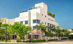 Valkoinen moderni rakennus, jossa on siniset ikkunapuitteet, ympärillä puita ja palmuja. (Tekoälyn luoma teksti)