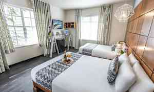 Hotellihuone, jossa kaksi parisänkyä, tyylikäs sisustus ja koristeelliset yksityiskohdat. (Tekoälyn luoma teksti)