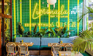 Ravintolan sisustus vihreillä kaakeloiduilla seinillä, neonkylttejä, palmuja, puupöytiä ja punottuja tuoleja. (Tekoälyn luoma teksti)