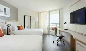 Moderni hotellihuone, jossa on kaksi suurta sänkyä, kirjoituspöytä ja tuoli sekä parveke merinäköalalla. (Tekoälyn luoma teksti)