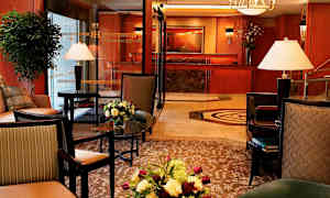 Tyylikkäästi sisustettu hotellin aulahenkinen tila, jossa on kalustettuja istuimia, sisustuselementtejä, kukka-asetelmia ja vastaanotto taustalla. (Tekoälyn luoma teksti)