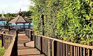 Puiset kävelysillat johtavat järven rannalla olevaan paviljonkiin, jota ympäröivät vihreät lehdet. (Tekoälyn luoma teksti)