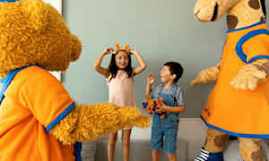 Kaksi lasta vuorovaikuttaa karhu- ja kirahvimaskotin kanssa ja näyttää nauttivan. (Tekoälyn luoma teksti)