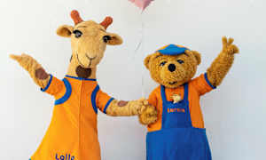 Kirahvi ja nallehahmo vaatteissa tekevät iloisia eleitä valkoista taustaa vasten. (Tekoälyn luoma teksti)