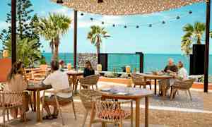 Ulkoilmaravintola, jossa pöytiä ja tuoleja merimaiseman edessä. (Tekoälyn luoma teksti)